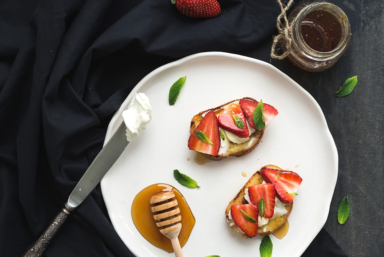 French toasts with strawberry, cream cheese, honey and mint on light ceramic plate over black backdrop