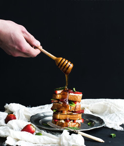 French toasts tower with strawberry cream cheese and mint hand is pouring honey over top of it