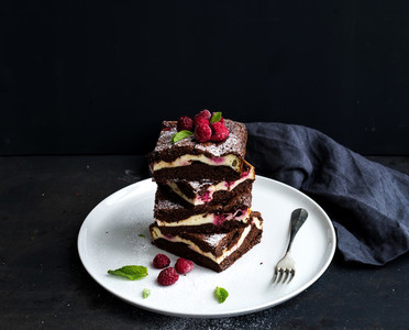 Brownie cheesecake tower with raspberries on white plate black backdrop copy space