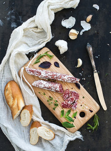 Meat gourmet snack  Salami  garlic  baguette and herbs on rustic wooden board over dark grunge backdrop