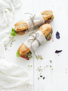 Sandwiches with beef  fresh vegetables and herbs over white wood backdrop  copy space