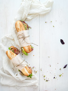 Sandwiches with beef fresh vegetables and herbs over white wood backdrop copy space
