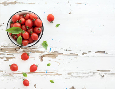 Cherry tomatoes in metal bowl and fresh basil leaves on rustic white wooden backdrop  top view