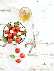 Caprese salad cherry tomatoes and mozzarella in metal bowl with olive oil on rustic white wooden backdrop  top view