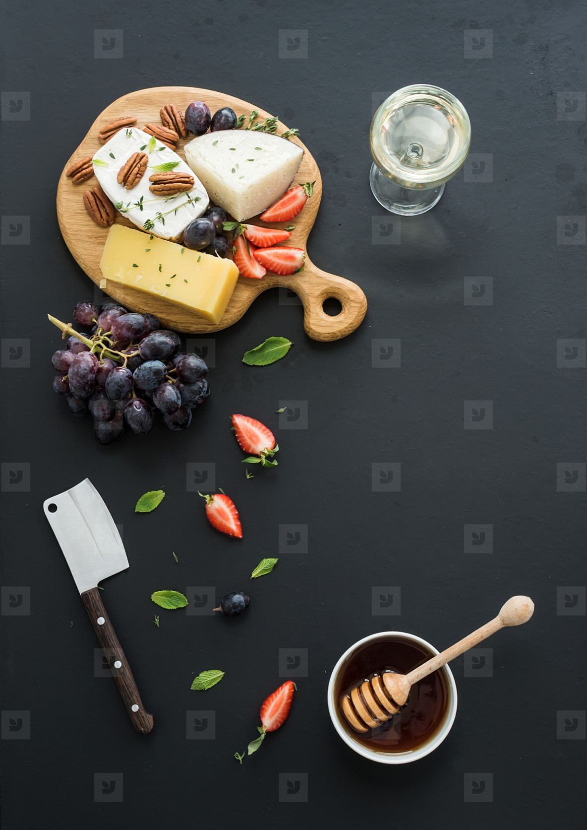 Cheese appetizer selection or whine snack set  Variety of cheese  grapes  pecan nuts  strawberry and honey on round wooden board over black backdrop  top view