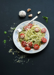 Pasta spaghetti with pesto sauce  basil  garlic  baked cherry tomatoes on rustic dark table  top view