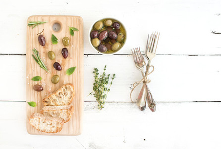 Mediterranean olives with herbs and ciabatta slices on rustic wooden board  over white background top view