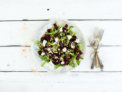 Beetroot salad with arugula  feta cheese  red salt and pumpkin seeds in vintage plate over white rustic wooden background  top view