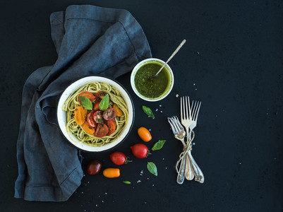 Pasta spaghetti with pesto sauce  basil  slow roasted cherry tomatoes in rustic metal bowl on dark grunge backdrop  top view