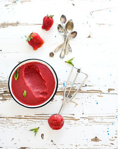 Strawberry sorbet or ice cream with fresh berries  mint and metal scooper on over white rustic wooden backdrop  top view