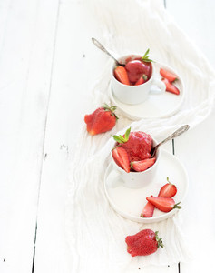 Strawberry sorbet ice cream with mint leaves in cups over rustic white wooden background top view