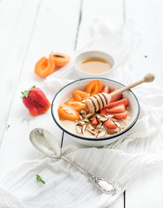 Healthy breakfast set Rice cereal or porridge with fresh strawberry apricots almond and honey over white rustic wood backdrop top view