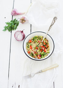 Healthy bulgur salad with paprika  red onion  parsley and garlic in rustic metal bowl  Vintage silverware  white wooden backdrop  top view