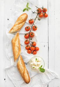 Baguette with banch of cherry tomatoes  basil and mozzarella cheese on rustic white wooden backdrop  top view