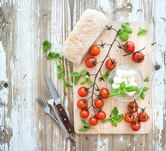 Ciabatta bread with banch of cherry tomatoes  basil and mozzarella cheese on rustic wooden board over old white backdrop  top view