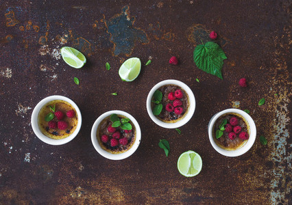 Creme brulees with raspberries and mint in white bowls over grunge metal backdrop  Top view