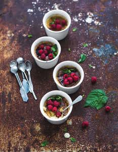 Creme brulees with raspberries and mint in white bowls over grunge metal backdrop  Top view