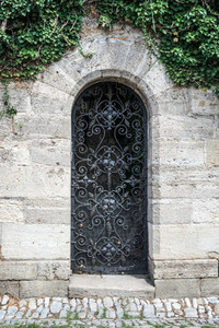 Old medieval black metal door with cerved bar and light stone wall