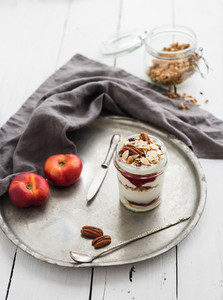 Yogurt oat granola with berries  honey  nuts and nectarins in glass jar on vintage metal tray over rustic white  background