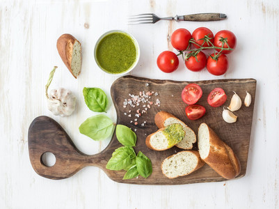 Pesto sauce  bread  cherry tomatoes  fresh basil and garlic on rustic walnut chopping board over white wooden backdrop