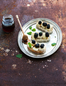 Italian bruschetta sandwich with brie cheese honey and blackberry on vintage silver tray over grunge rusty metal background top view