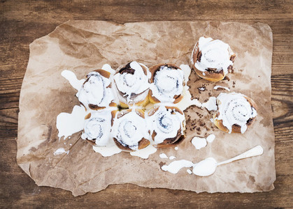 Cinnamon rolls with cream cheese icing on piece of oily craft paper over rustic wooden background