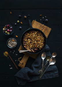 Healthy breakfast Oat granola crumble with frozen fresh berries and seeds in irom skillet pan on rustic wooden board over dark backdrop