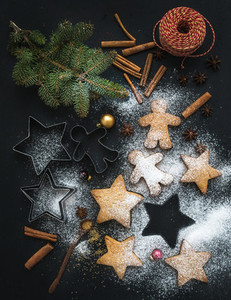 Cooked Christmas holiday traditional gingerbread cookies with sugar powder anise and cinnamon sticks on black background