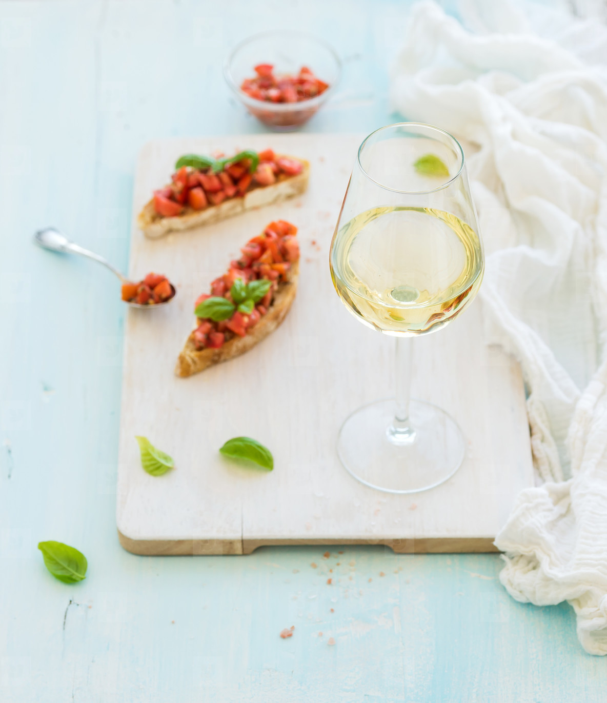 Glass of white wine, tomato and basil bruschetta sandwich on painted wooden serving board over rustic blue background