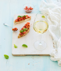 Glass of white wine  tomato and basil bruschetta sandwich on painted wooden serving board over rustic blue background