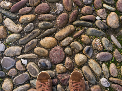 Feet in brown sneakers on the old medieval stone pavement