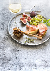 Wine appetizer set Glass of white wine honeycomb with drizzlier figs grapes melon and prosciutto on silver tray over rustic grunge surface