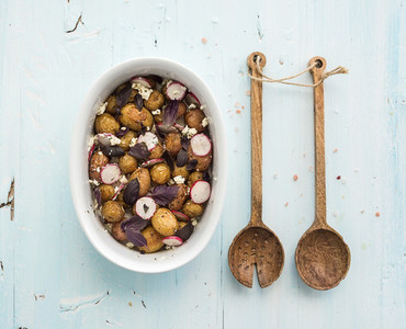 Roast young potato salad with radish and soft cheese in a baking dish over light blue background