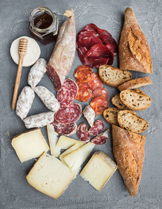 Cheese and meat appetizer selection or wine snack set  Variety of italian cheese  salami  bresaola  baguette  honey on over grey concrete backdrop  top view