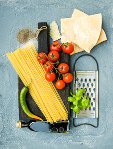 Ingredients for cooking pasta  Spaghetti  Parmesan cheese  cherry tomatoes  metal grater  olive oil and fresh basil on grey blue concrete background