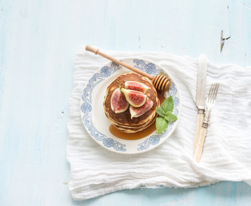 Pancake tower with fresh figs and honey on a rustic plate Light blue  background
