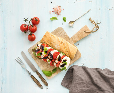 Tomato mozzarella and basil sandwich on wooden chopping board over light blue background top view