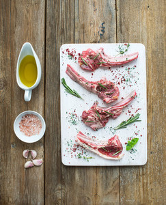 Raw lamb chops Rack of Lamb with garlic rosemary and spices on white chopping board oil in a saucer salt dinnerware over rustic wood background