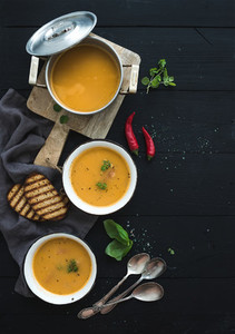 Red lentil soup with spices  herbs  bread in a rustic metal saucepan and bowls  over dark wood backdrop  top view