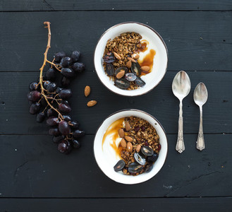 Healthy breakfast set  Bowls of oat granola with yogurt  fresh grapes  almond and  honey over black wooden backdrop
