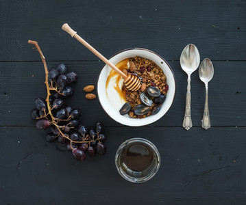 Healthy breakfast set  Bowl of oat granola with yogurt  fresh grapes  almond and  honey over black wooden backdrop