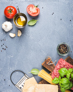 Ingredients for cooking pasta Bolognese  Spaghetti  Parmesan cheese   tomatoes  metal grater  olive oil  garlic  minced meat and fresh basil on grey concrete background  top view