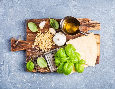 Ingredients for cooking Pesto sauce Parmesan cheese metal grater fresh basil olive oil garlic and pine nuts on old rustic wooden board over grey concrete background