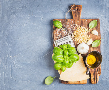 Ingredients for cooking Pesto sauce  Parmesan cheese  metal grater  fresh basil  olive oil  garlic and pine nuts on old rustic wooden board over grey concrete background