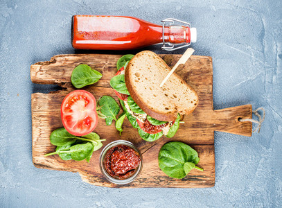 Chicken  sun dried tomato and spinach sandwich with spicy sauce on rustic wooden board over grey concrete textured background