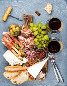 Cheese and meat appetizer selection or wine snack set  Variety of cheese  salami  prosciutto  bread sticks  baguette  honey  grapes  olives  sun dried tomatoes  pecan nuts over grey concrete textured
