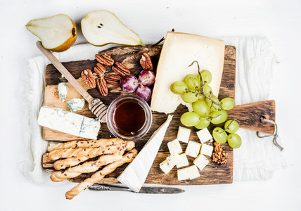Cheese appetizer set  Various types of cheese  honey  grapes  pear  nuts and bread grissini sticks on rustic wooden board over white background