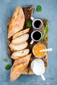 Breakfast set Baguette orange jam and coffee in cups on rustic wooden board over concrete grey blue background
