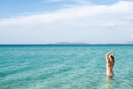Back of beautiful woman wearing blue bikini standing in the water on Mediterranean sea coast Cesme Ilica beach Turkey