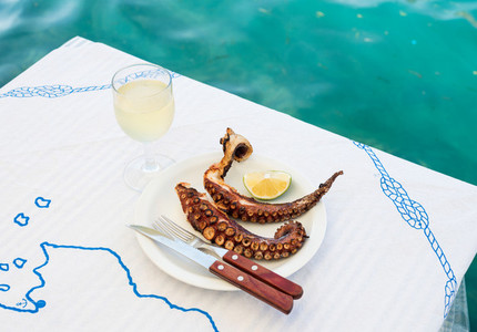 Grilled octopus and white wine glass on a table at the sea coast